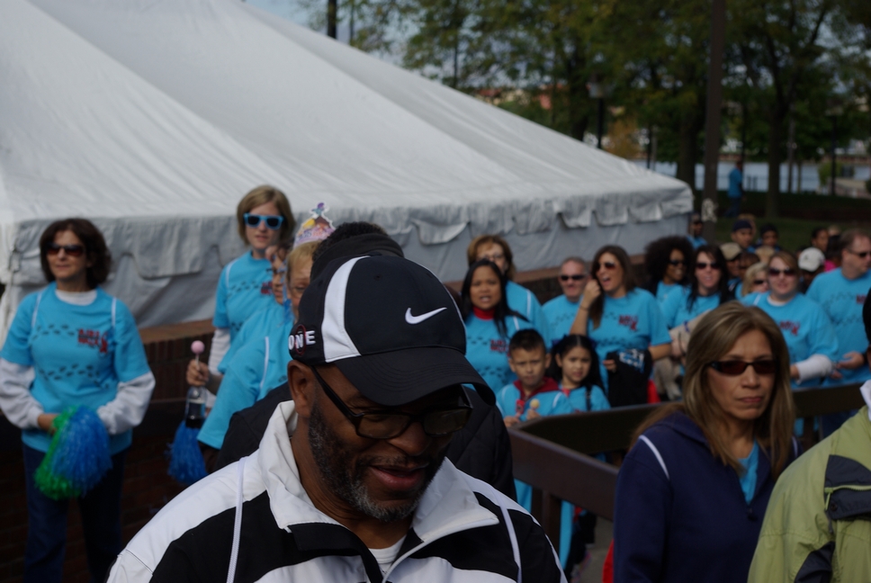 a man is wearing a hat and black sunglasses with people in blue shirts behind him