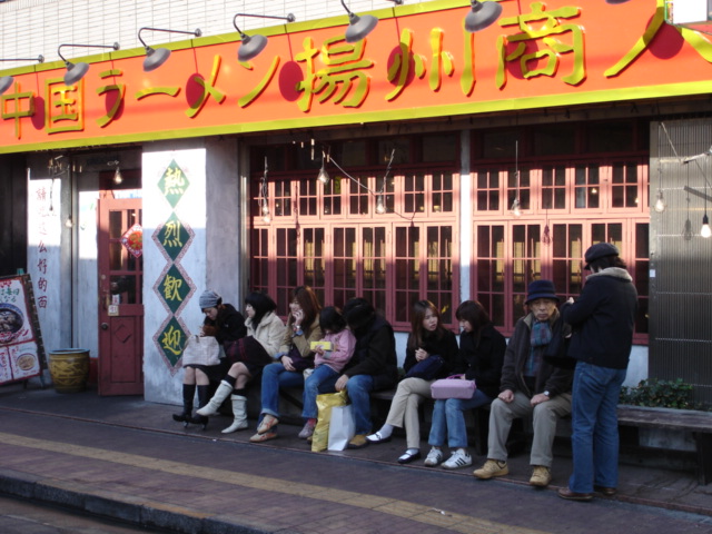 many people sitting on benches outside of a chinese restaurant
