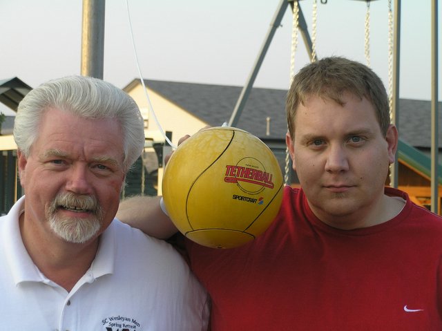 two men pose with a yellow ball on their shoulder