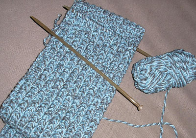 two crocheted yarns and knitting needle laying next to each other