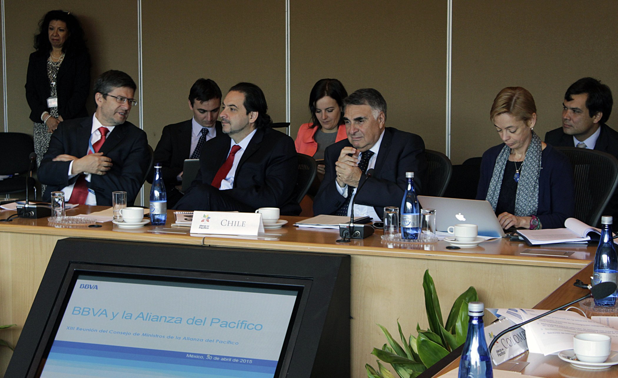 men and women wearing suits sit around a conference table