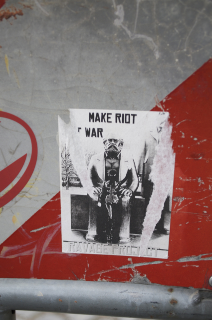 a sticker on a post reads make riot war
