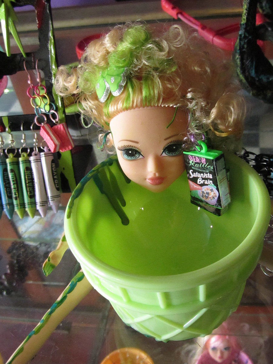 an odd plastic doll head with a green wig and neon green eyes and curls sits inside a glass bowl