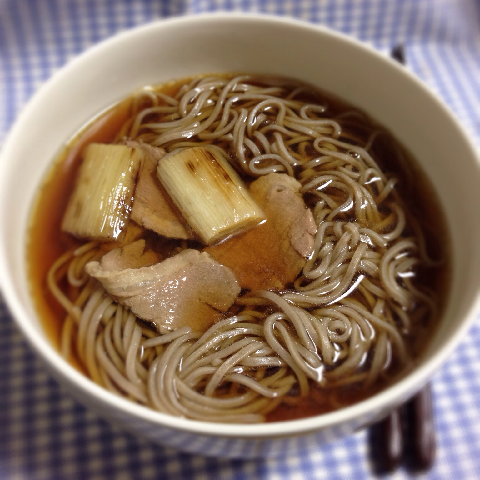 a bowl of noodles, pork and mushroom soup on a checkered cloth