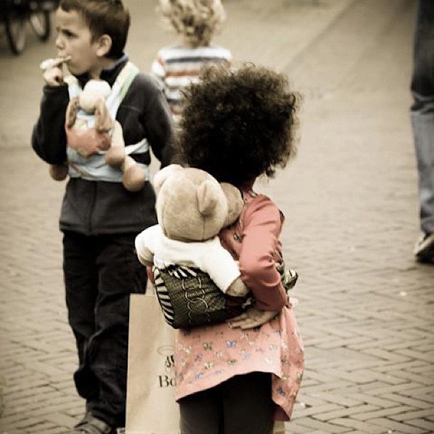 young children carry stuffed animals as they walk down the street