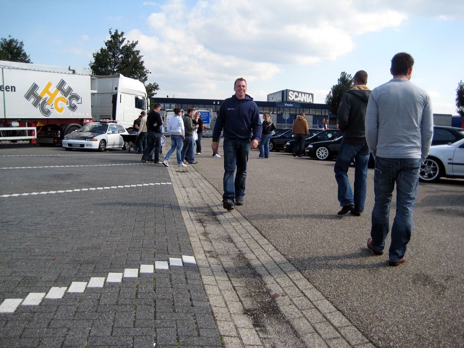 several people are walking along a lot as other cars