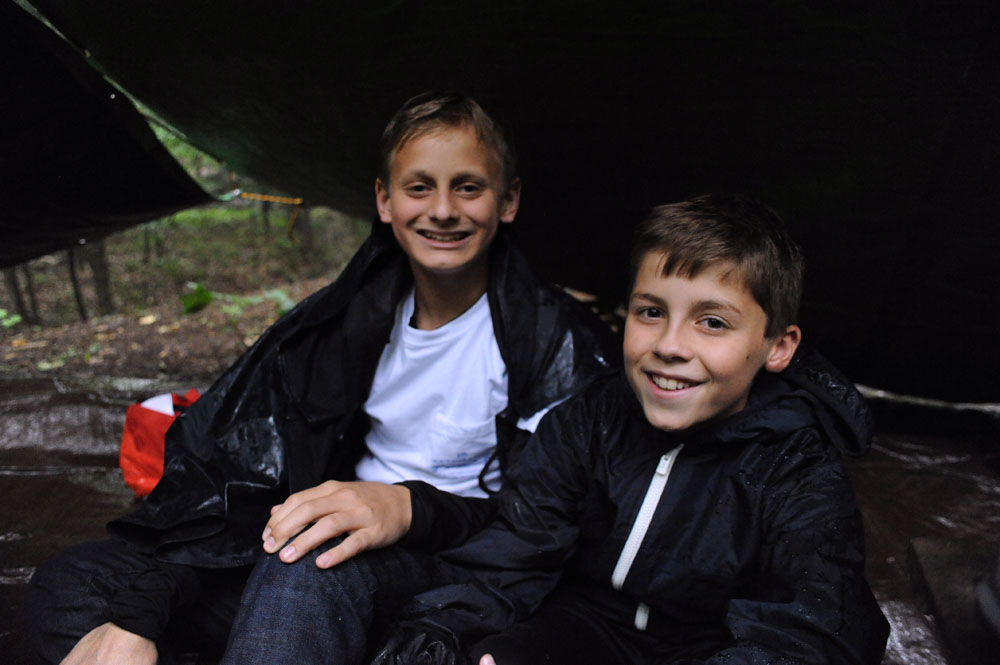 two boys smile and sit together in a tent