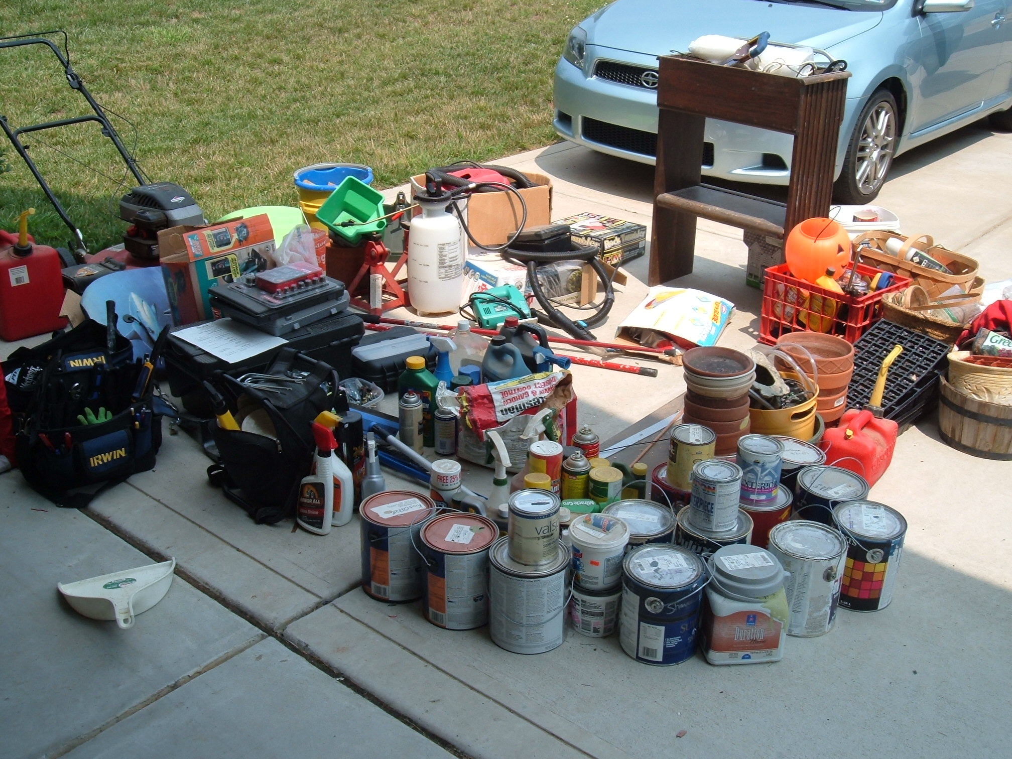 an assortment of paint cans sitting on the ground with other things and a car parked near them