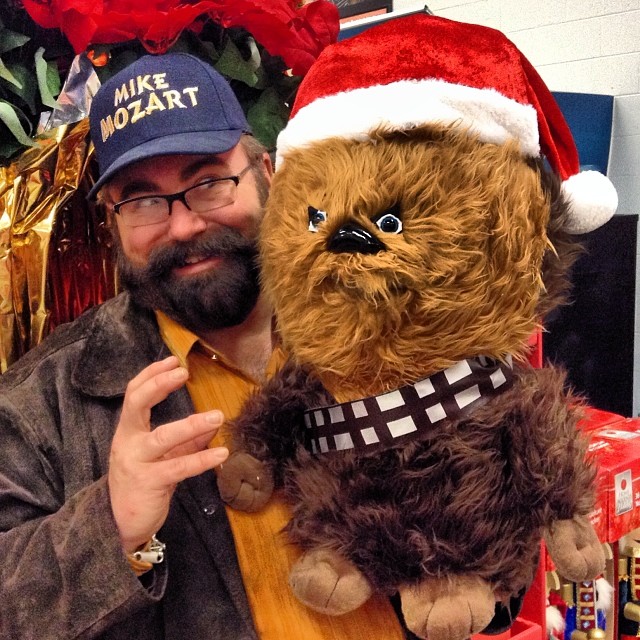 a bearded man in a santa hat holding a teddy bear wearing a shirt with a star wars cap