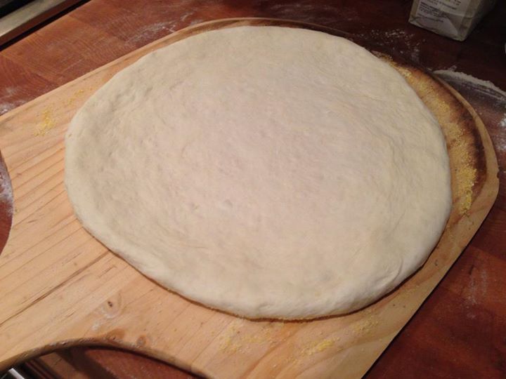 a round pizza dough sitting on a wooden board