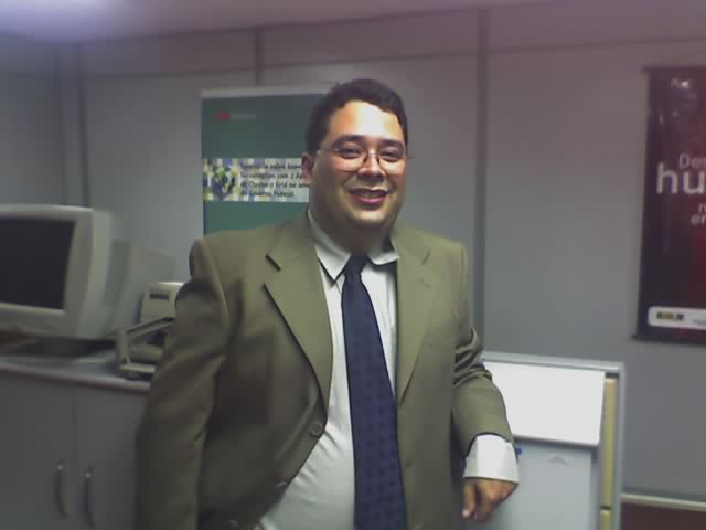 a man in business attire in an cubicle with a monitor and computer on the wall