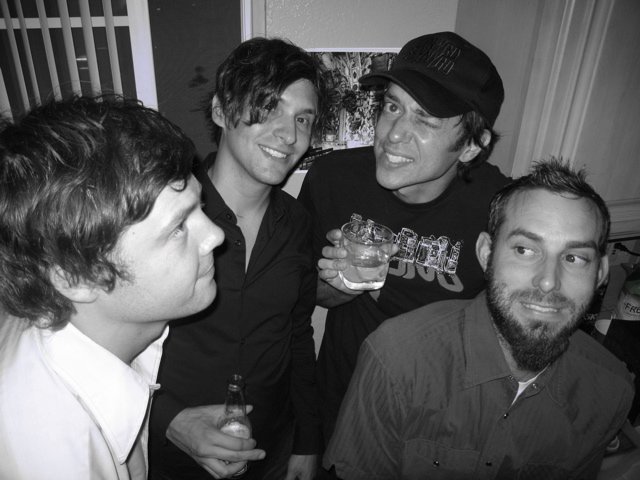 three men smile at the camera while having drinks