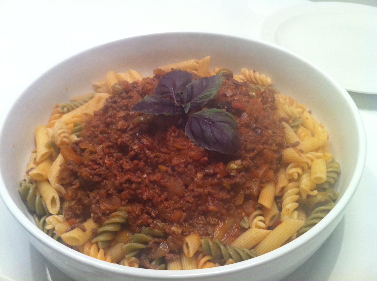 a bowl of pasta with meat sauce and leafy greens
