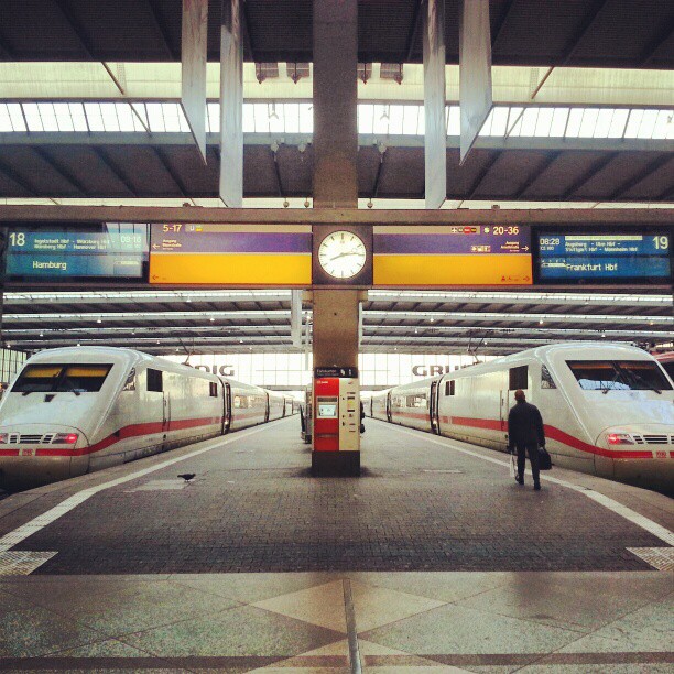 a man walks across the platform next to two commuter trains