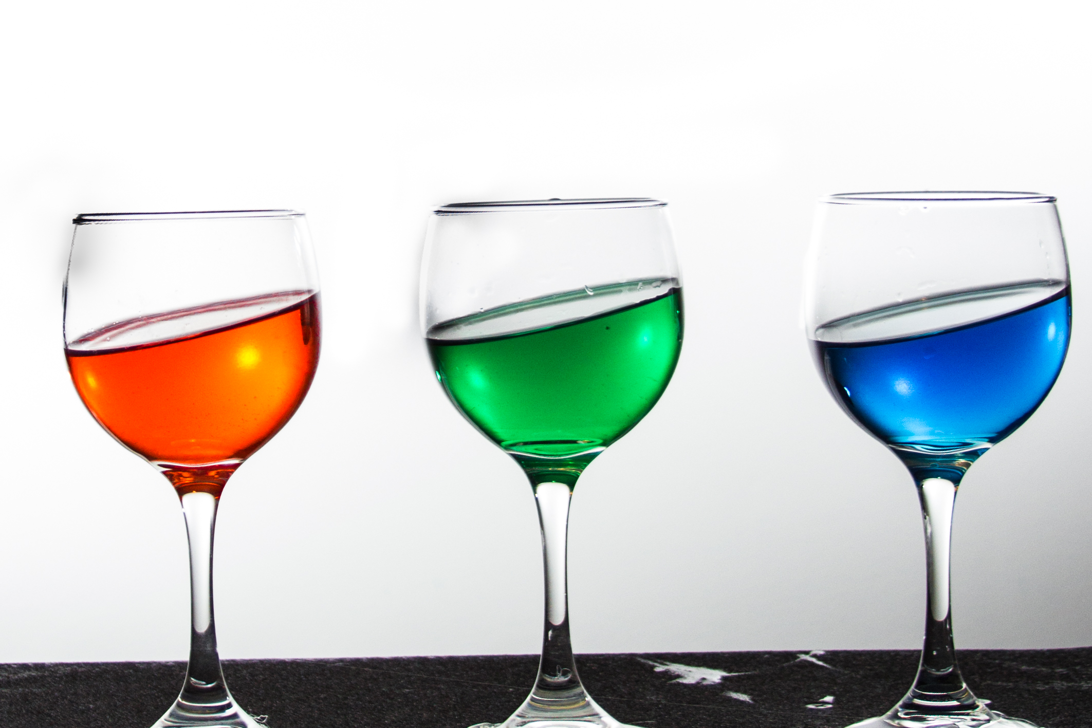 three wine glasses with different colored liquids in them