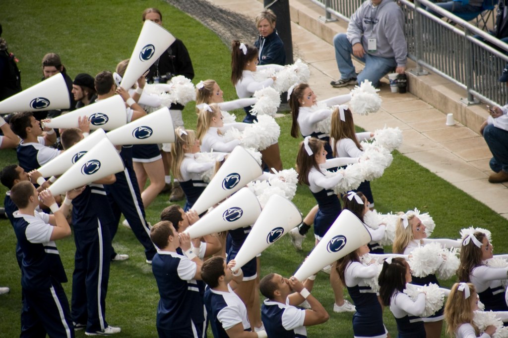 cheerleaders in blue uniforms holding large white speakers on the field