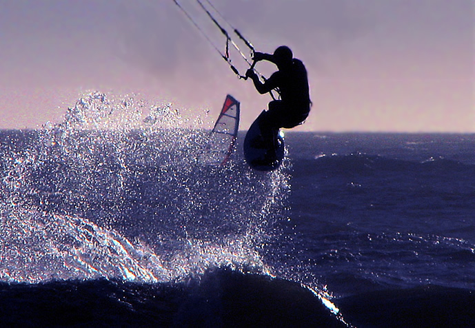 someone windsurfing in the ocean while a wave crashes