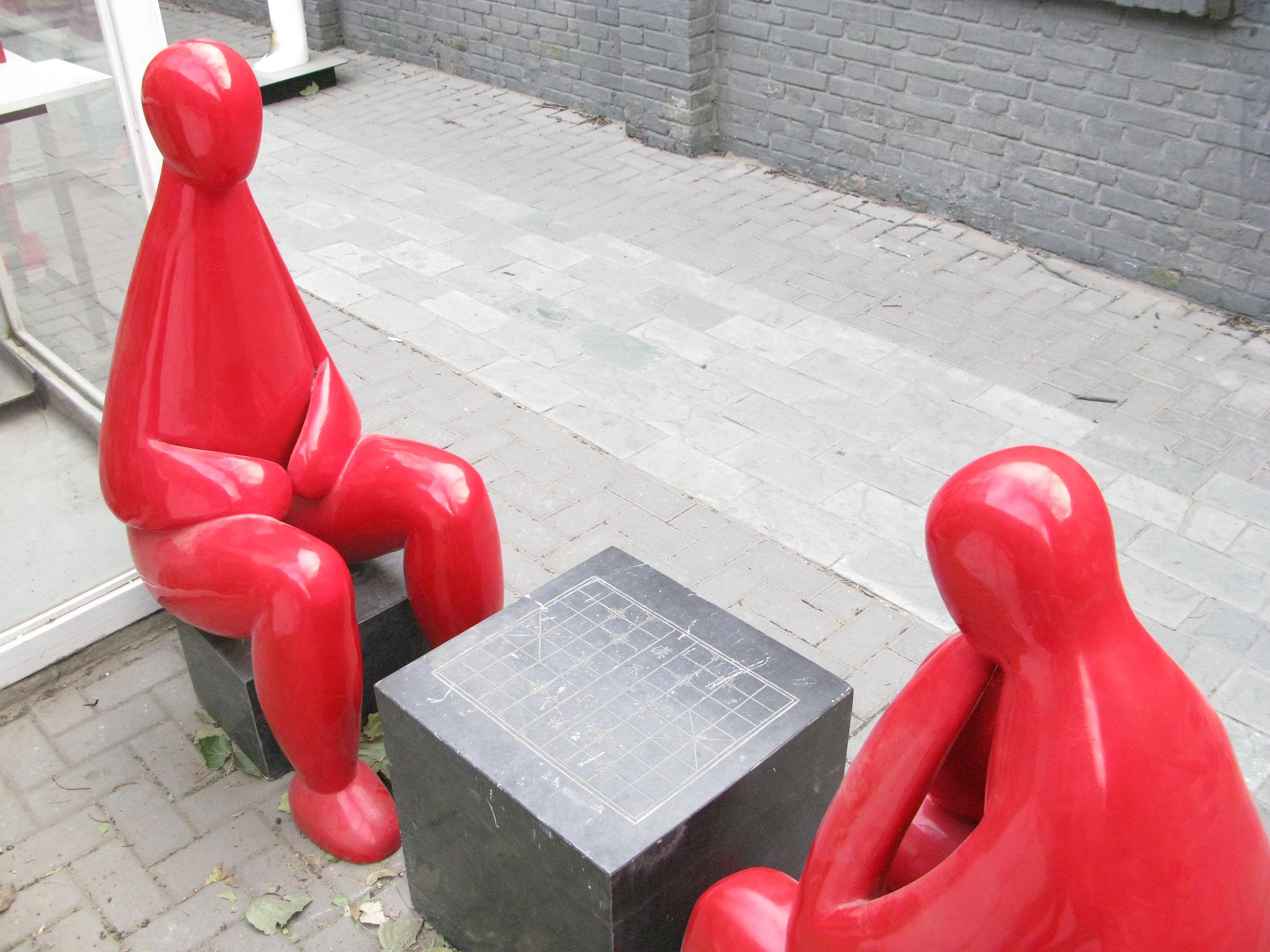 a red statue sitting next to a square black vase