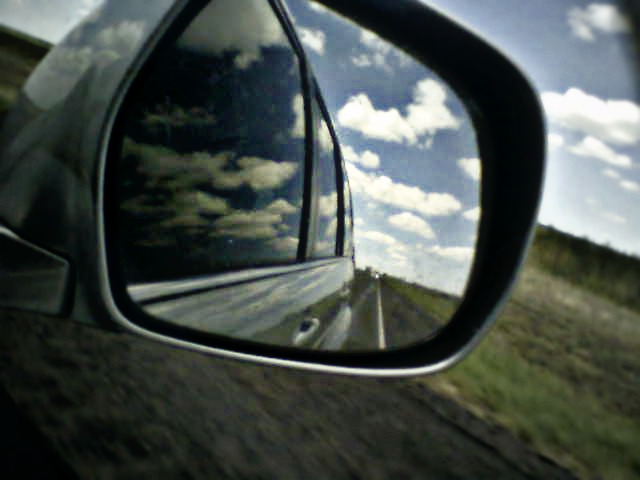 a rear view mirror reflecting a sky full of clouds