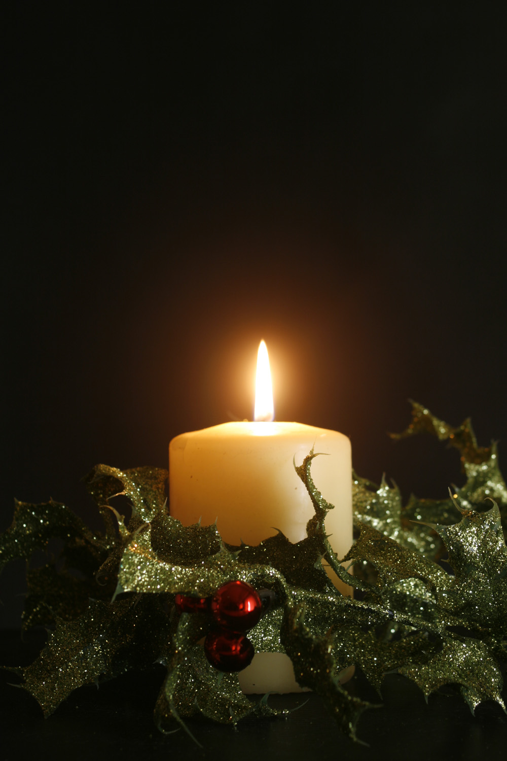 a white christmas candle surrounded by green holly wreath