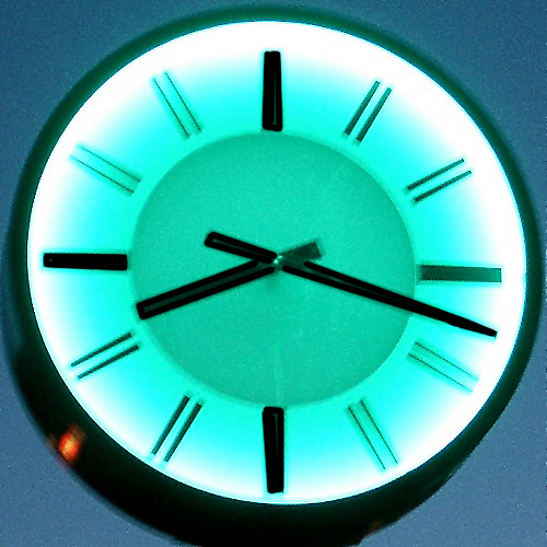 a clock with black hands is illuminated against a sky