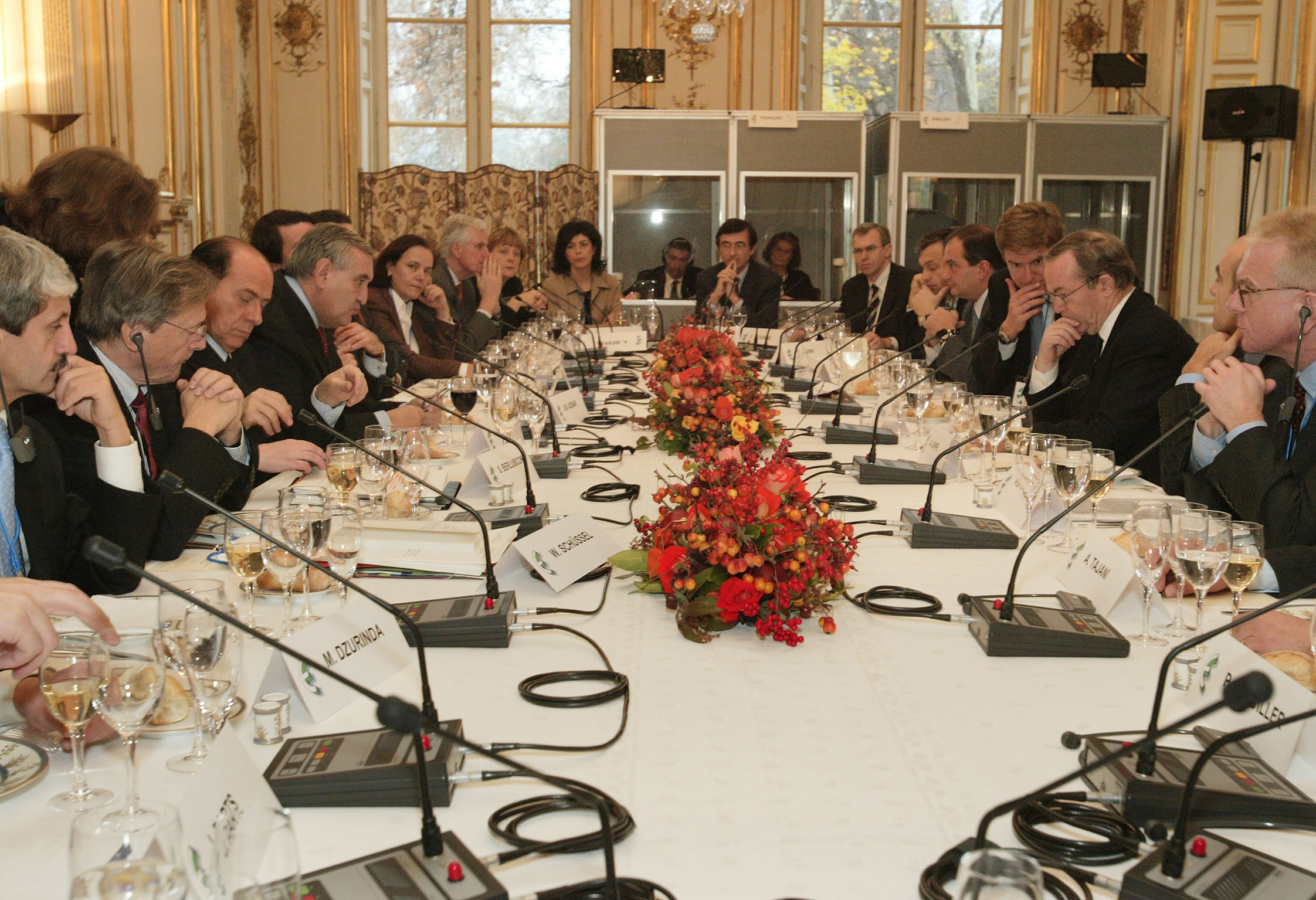 a group of men sitting at long table with phones and laptops in front of them