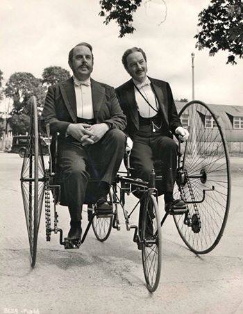 two people are riding on an old fashioned bicycle