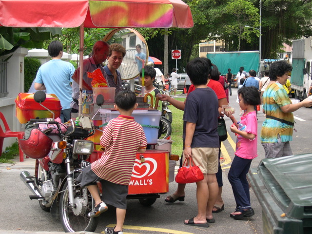 people gather around a small food cart on the sidewalk