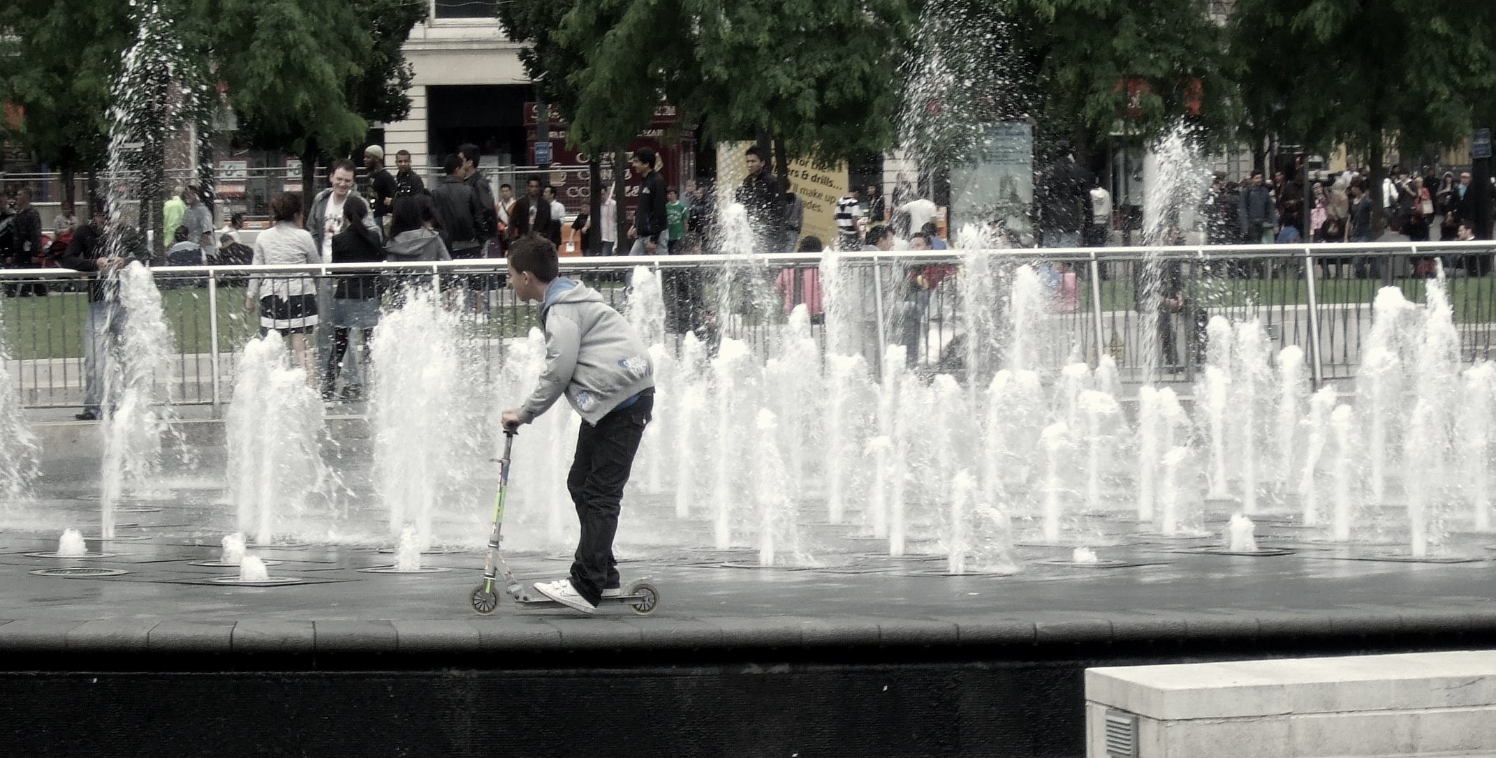 a boy stands on his skateboard by the water fountains in the city