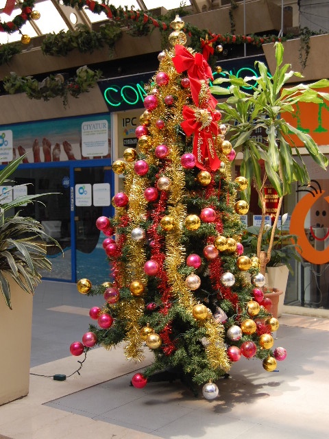 a tree decorated with ornaments and presents near a sidewalk