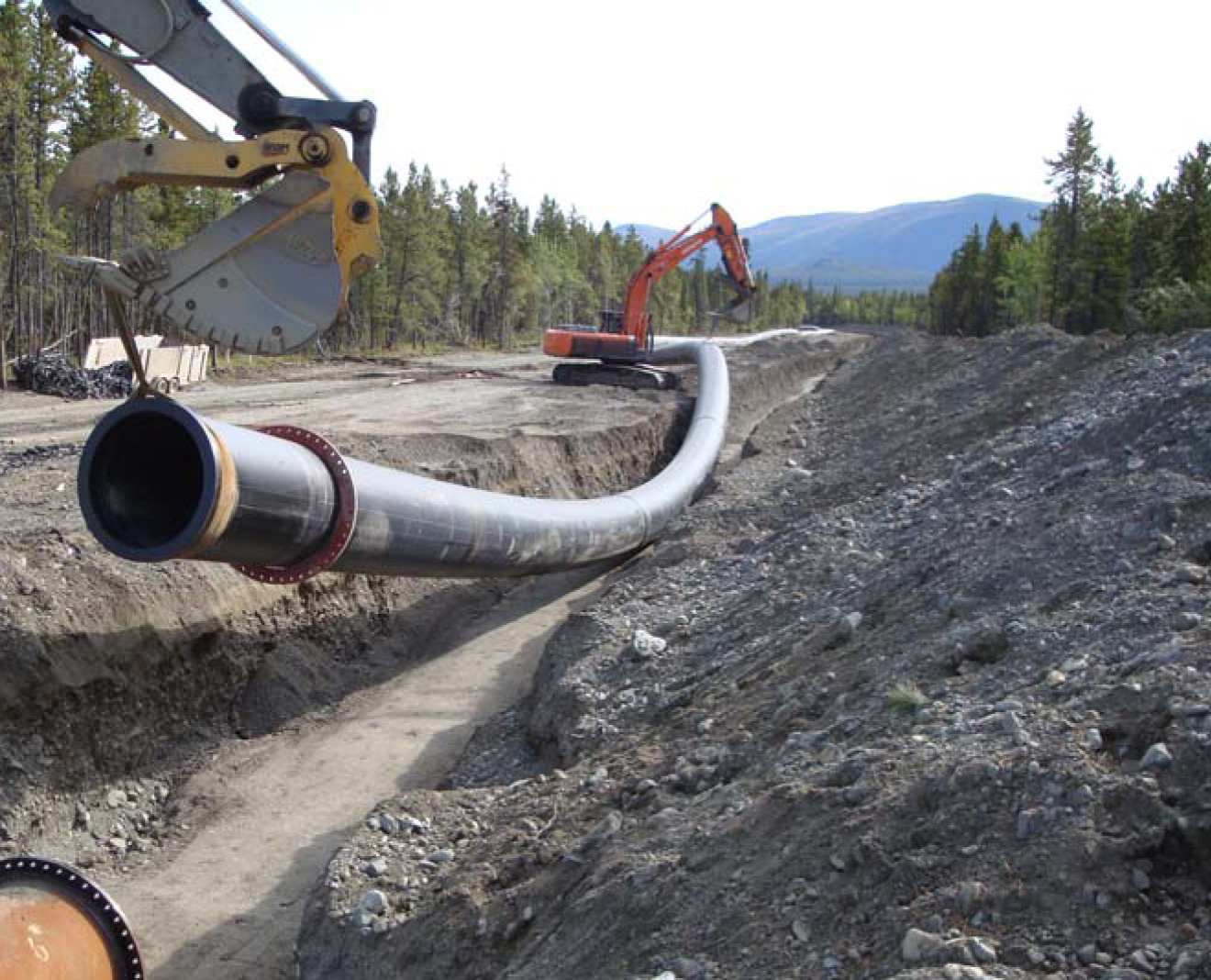 an excavator machine is placing pipe on a construction site