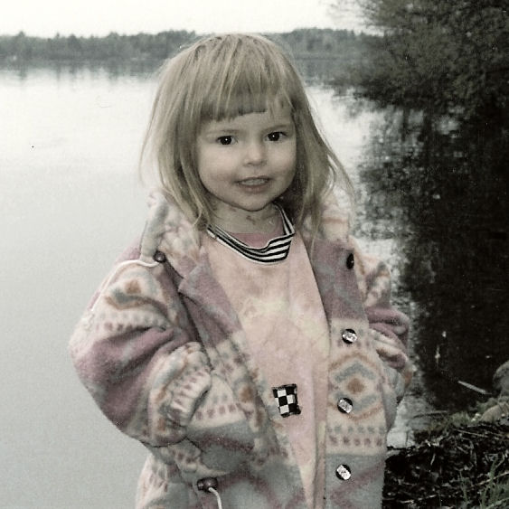 a child in a pink sweater is standing by the water