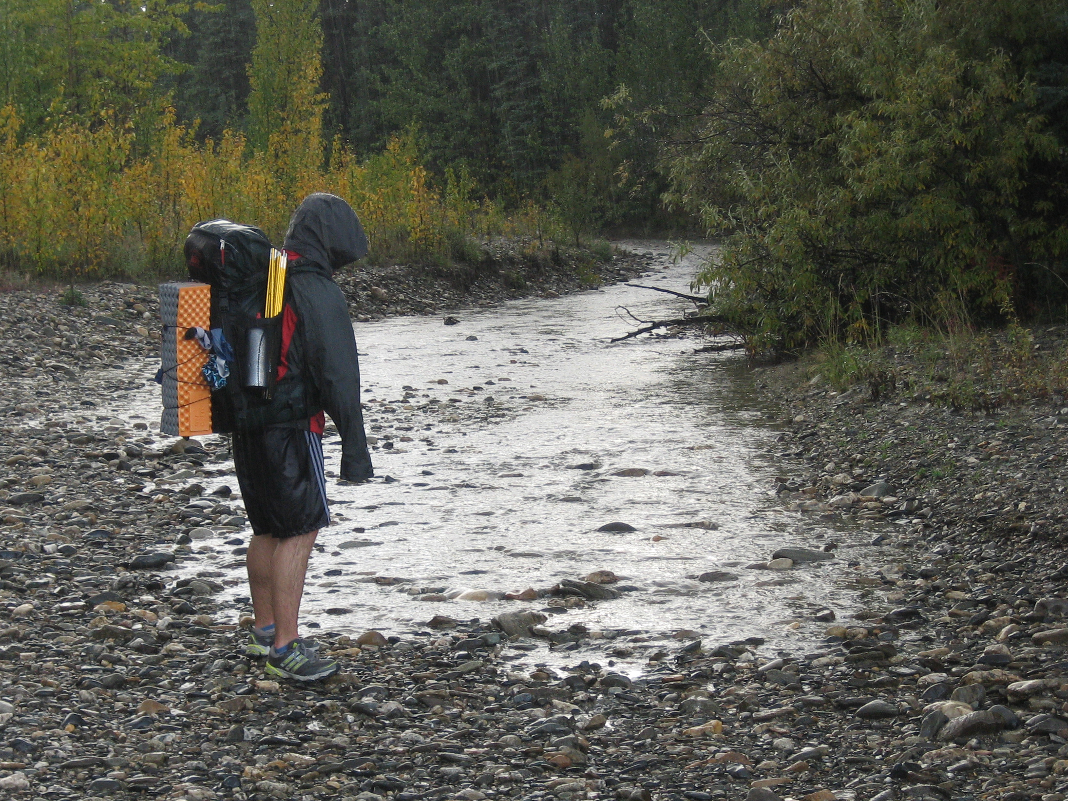 a man wearing backpack walks on a muddy path