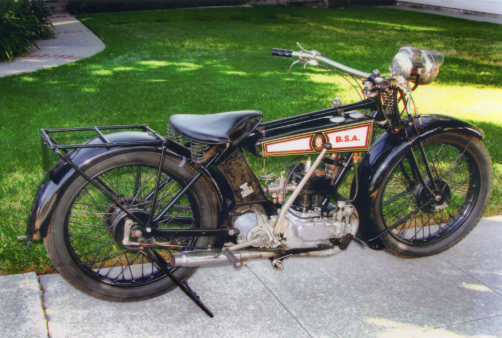 an old style motorcycle parked on the sidewalk near grass