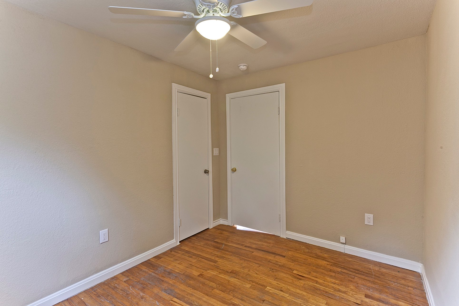 an empty room with wooden floors, ceiling fan and white doors