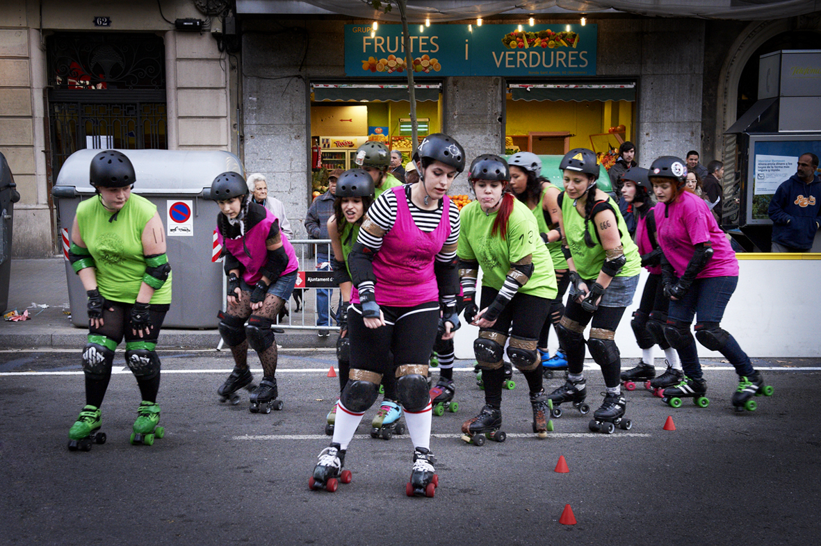 several women rollerblading down a street in front of a group of people