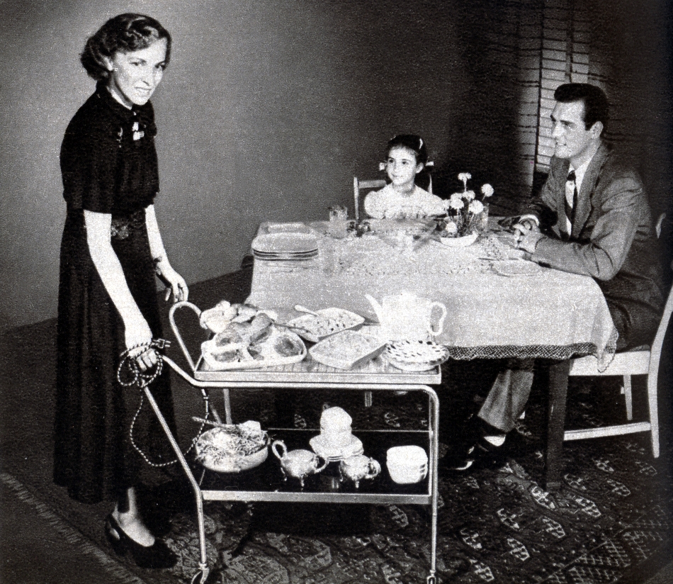 an old po with a woman ironing clothes, another man looks on and the girl at the table is setting the table