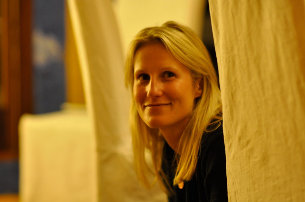 woman with long blond hair smiling by curtains