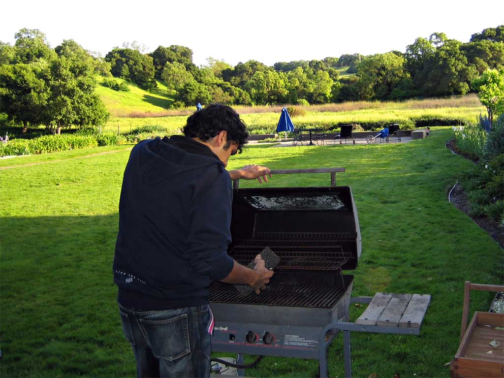 man standing on grass preparing to grill with barbecue grill in background