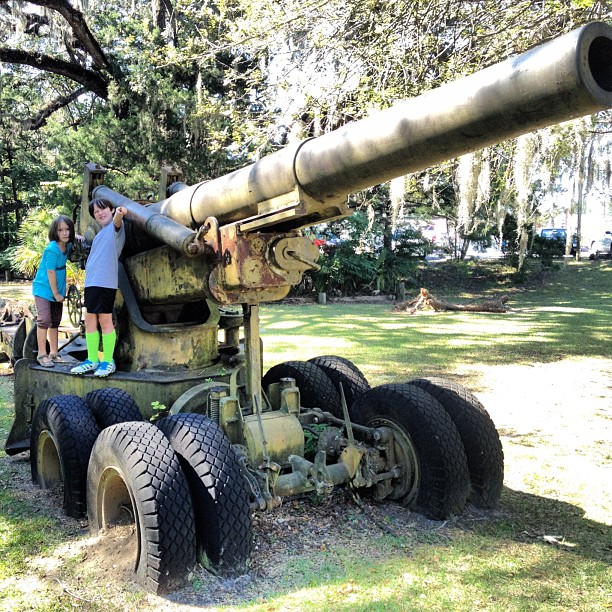 two children looking at the ground by a military gun