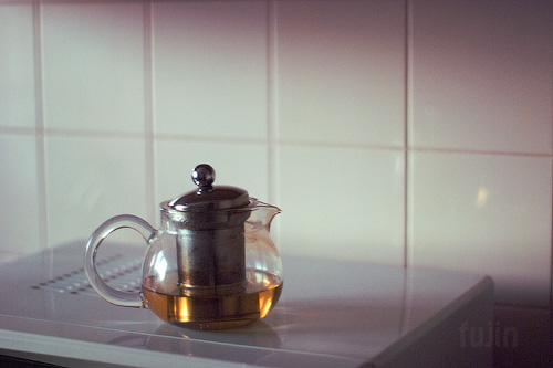 a glass teapot on the stove with light reflecting on it