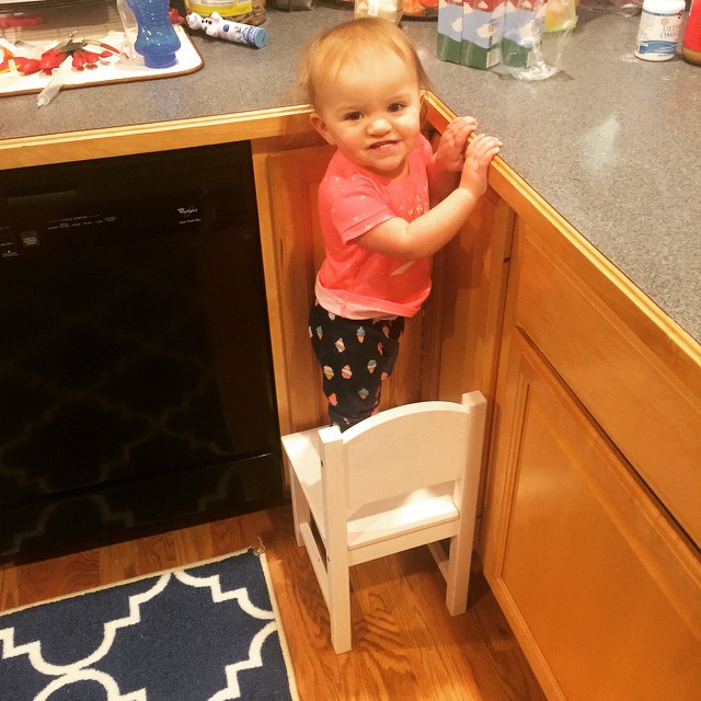 young child standing on small chair inside a kitchen