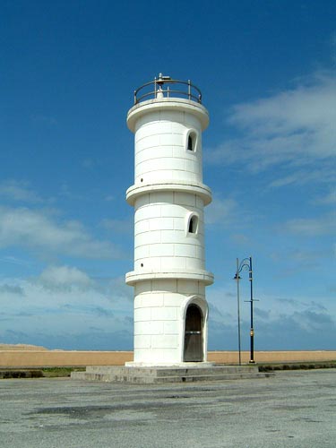 a tall white lighthouse with an ocean front and sky background