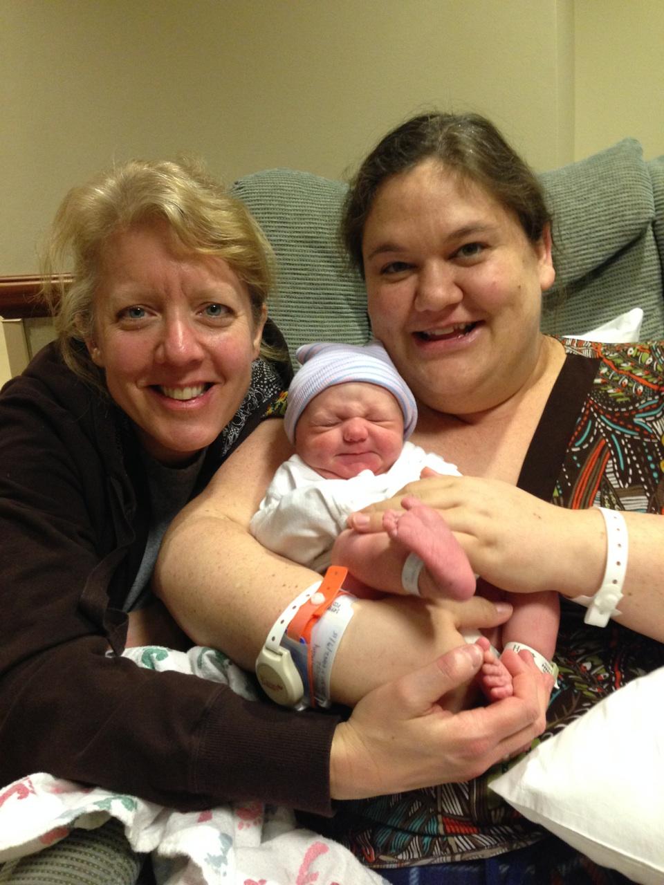 two women hold a newborn baby who is sitting in her lap