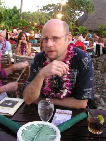 a man sits at an outdoor table while someone holds a plate