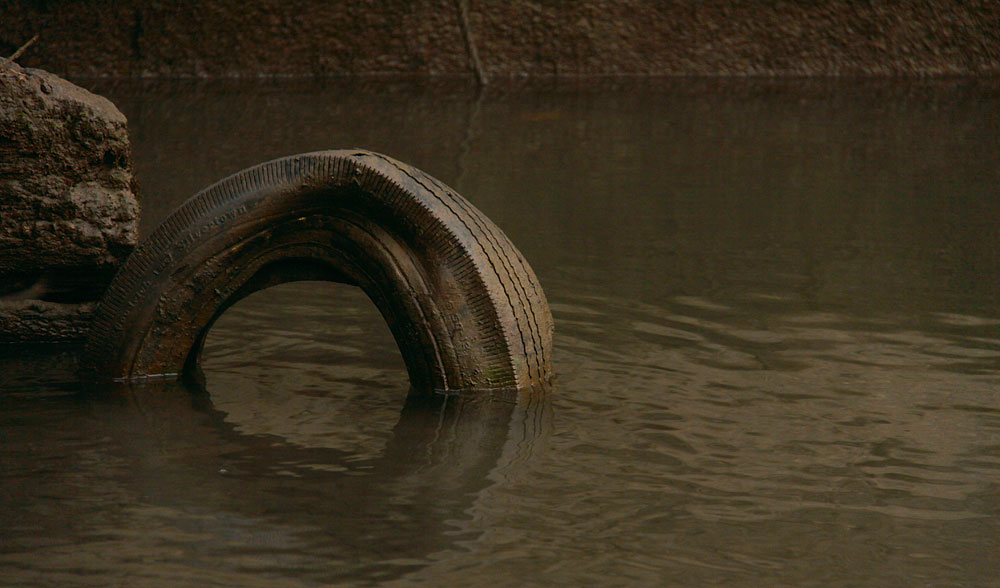 a tire stuck in the water beside a rock