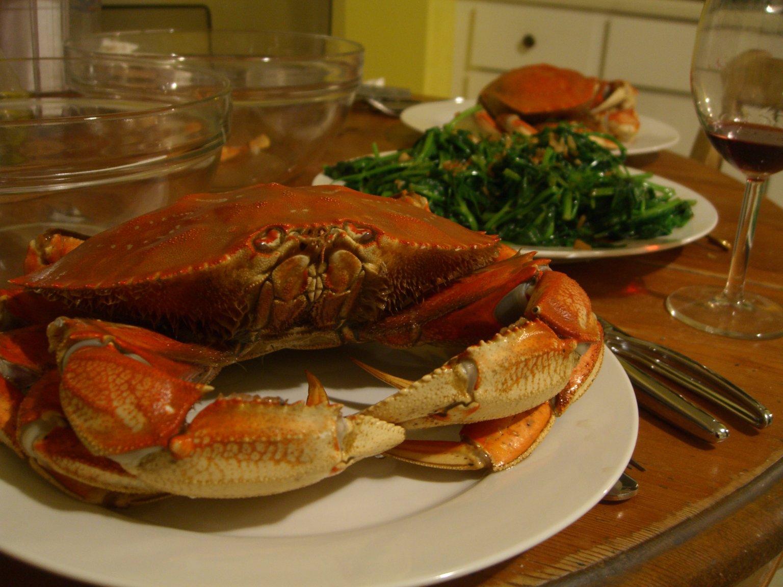 two cooked crabs on white plates with greens