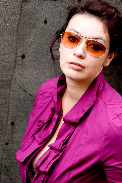 woman in purple shirt wearing sunglasses standing against a gray background
