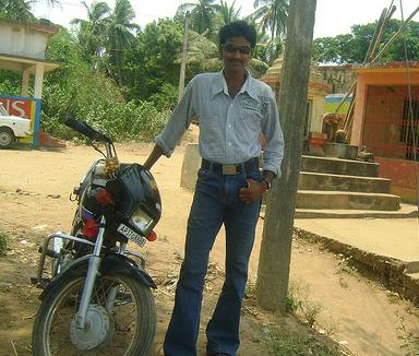 a man in a on down shirt poses with a parked motorcycle