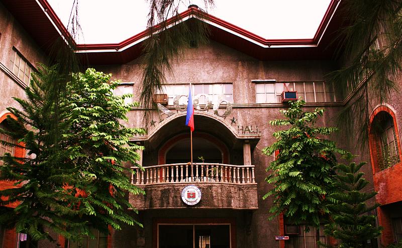 people are gathered in front of an apartment building with red roof and balconies